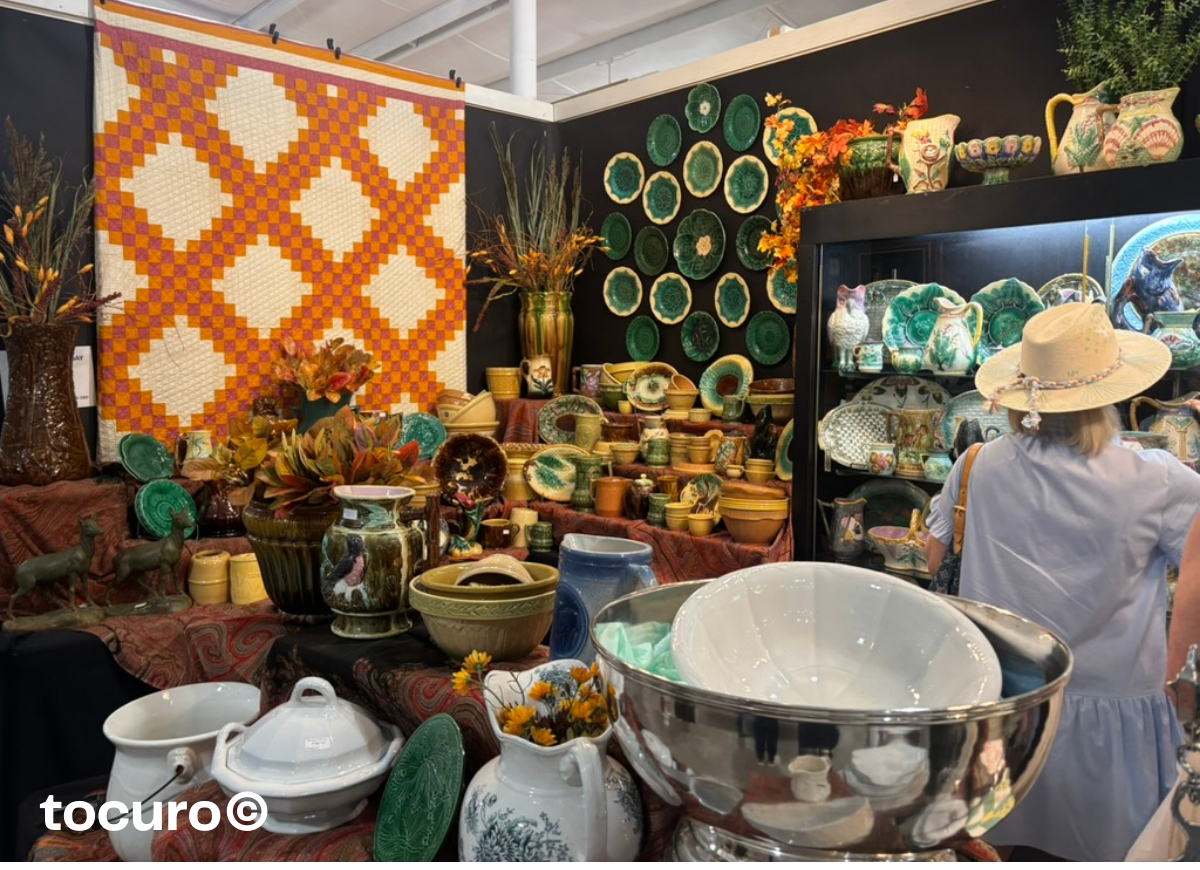 Vintage pottery and ceramic display at the Round Top Antiques Fair, featuring colorful bowls, plates, and quilts in a curated booth.